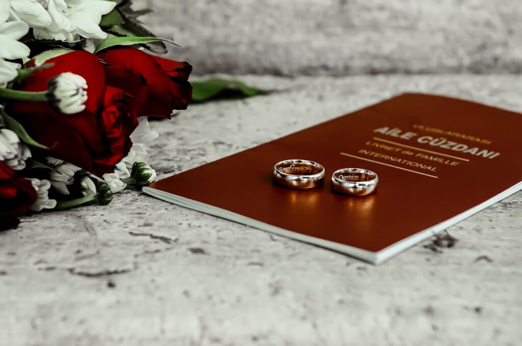 Silver wedding bands with red roses and a marriage booklet symbolize love and commitment.