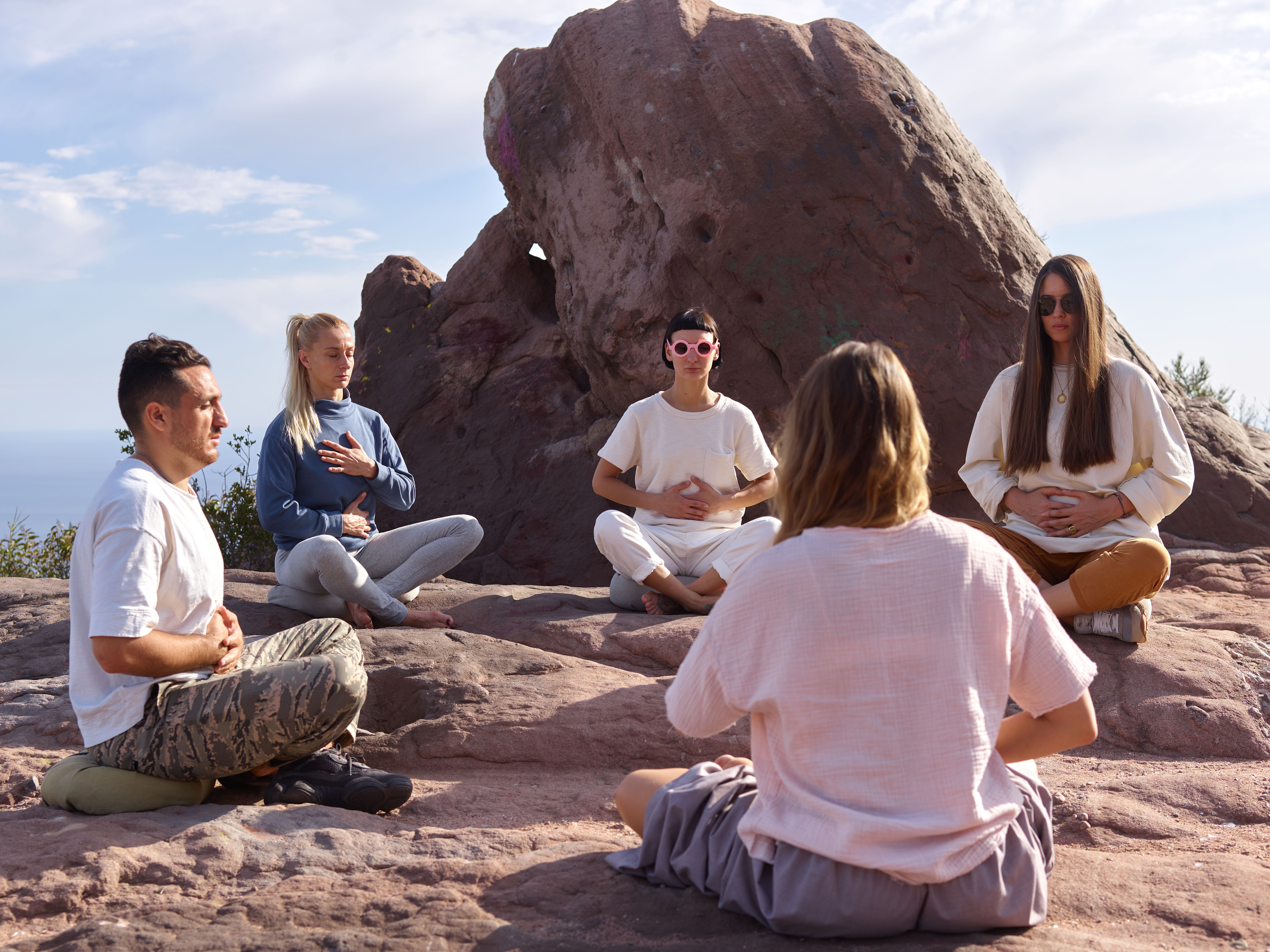 Five adults meditating outdoors on rocks, embracing a peaceful lifestyle.
