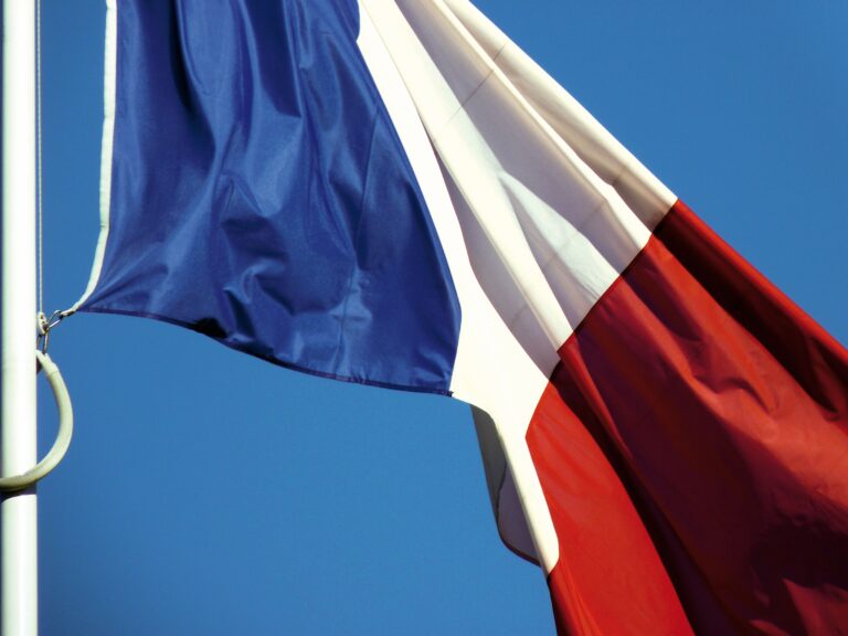 A close-up of the French national flag waving against a clear blue sky in Paris, France.